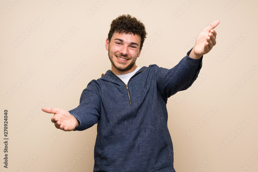 Man with curly hair over isolated wall presenting and inviting to come with hand Man with curly hair over isolated wall presenting and inviting to come with hand