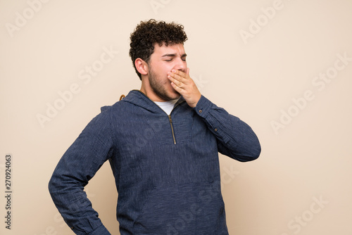 Man with curly hair over isolated wall yawning and covering wide open mouth with hand © luismolinero