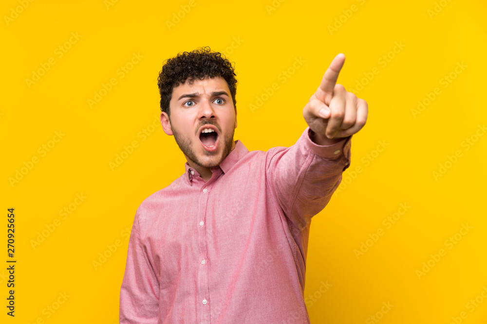 Fototapeta premium Man with curly hair over isolated yellow wall pointing away