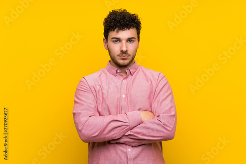 Man with curly hair over isolated yellow wall keeping arms crossed