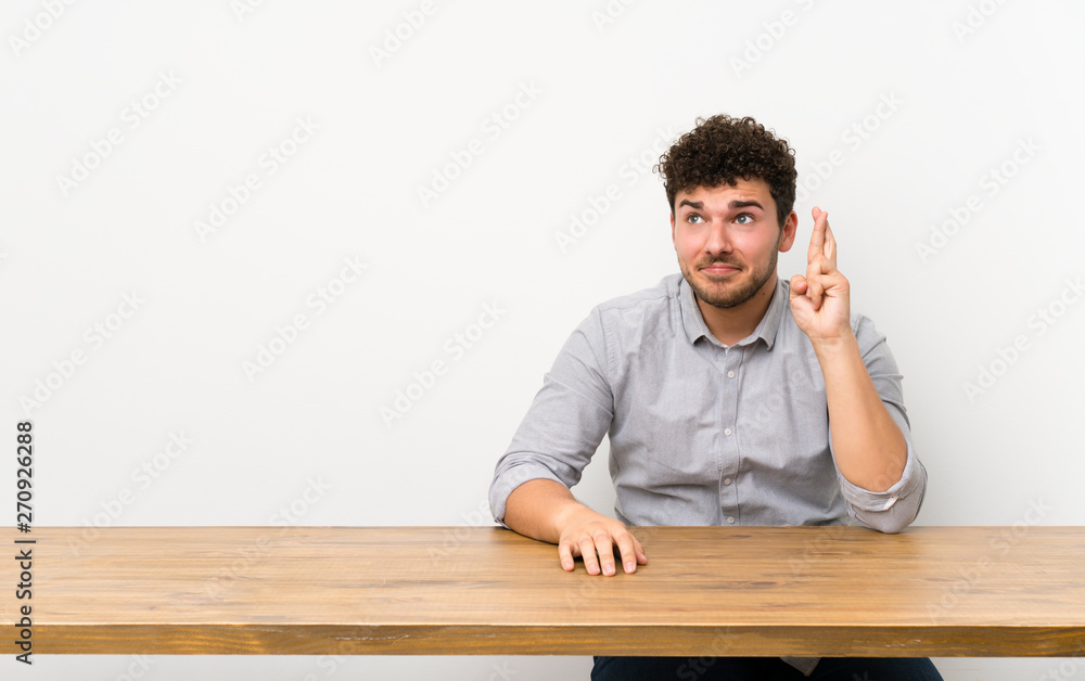 Young man with a table with fingers crossing and wishing the best Young man with a table with fingers crossing and wishing the best