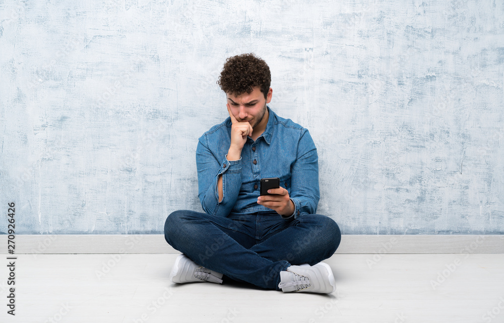 Young man sitting on the floor using mobile phone