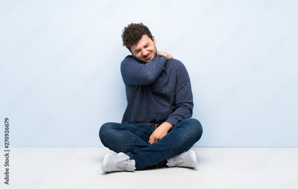 Young man sitting on the floor suffering from pain in shoulder for having made an effort Young man sitting on the floor suffering from pain in shoulder for having made an effort