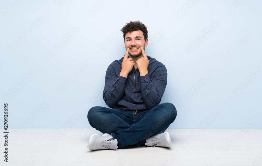 Young man sitting on the floor smiling with a happy and pleasant expression Young man sitting on the floor smiling with a happy and pleasant expression