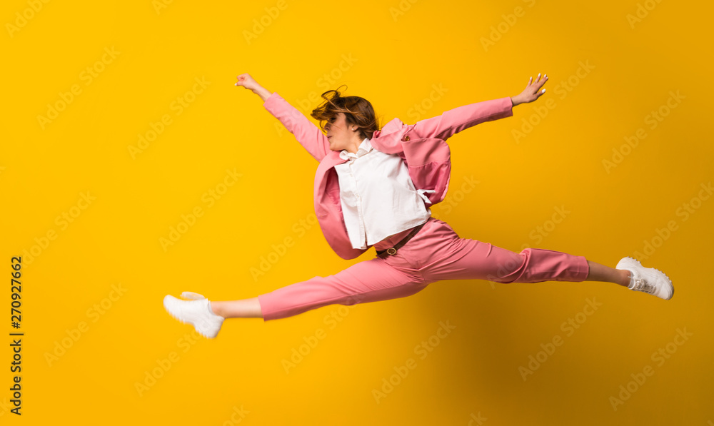 Young woman jumping over isolated yellow wall Young woman jumping over isolated yellow wall