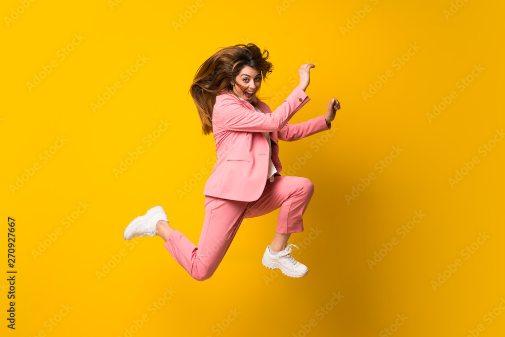 Young woman jumping over isolated yellow wall Young woman jumping over isolated yellow wall
