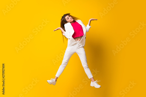 Young woman jumping over isolated yellow wall having doubts