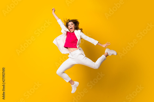 Young woman jumping over isolated yellow wall making victory gesture