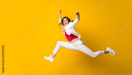Young woman jumping over isolated yellow wall