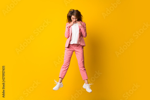 Young woman jumping over isolated yellow wall doing surprise gesture © luismolinero