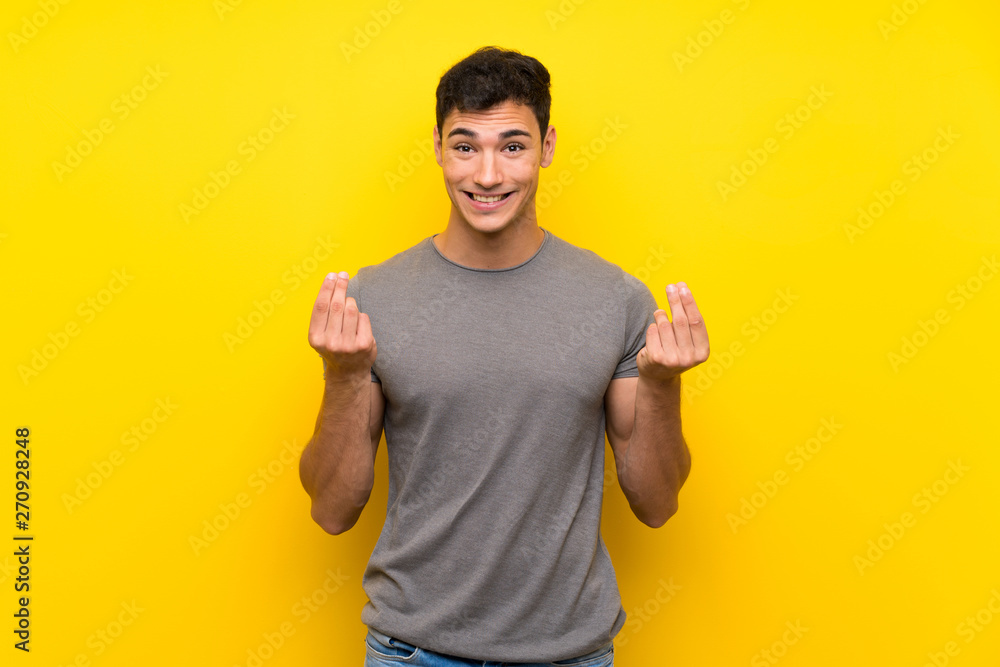 Handsome man over isolated yellow wall making money gesture Handsome man over isolated yellow wall making money gesture