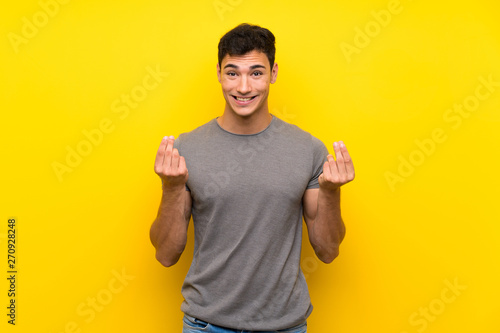 Handsome man over isolated yellow wall making money gesture