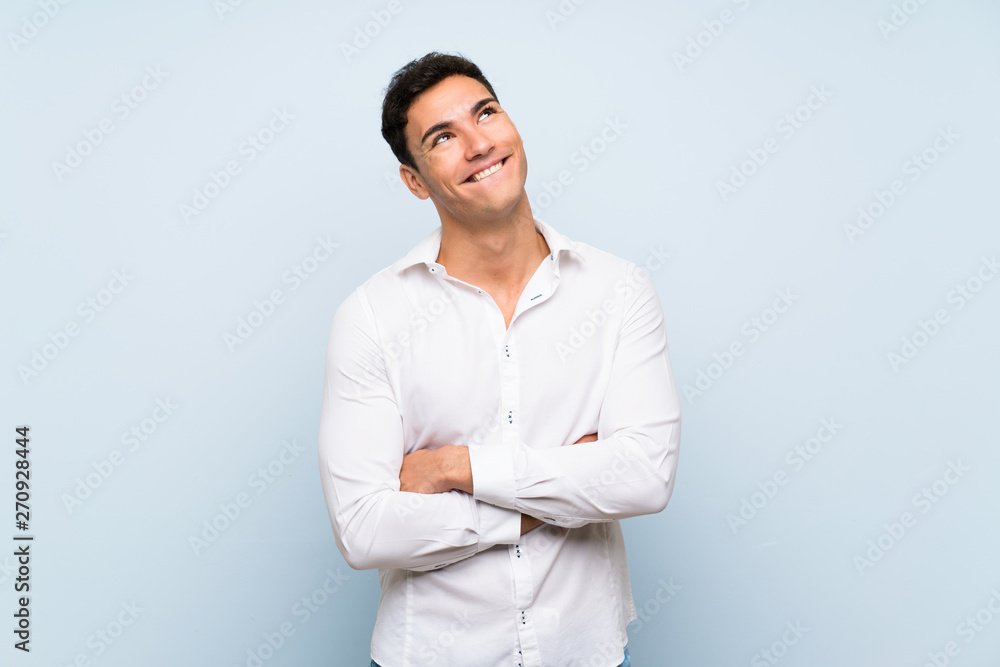 Handsome man over blue wall looking up while smiling Handsome man over blue wall looking up while smiling