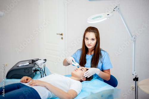 cosmetologist with a patient during facial procedures in a modern cosmetological and aesthetic clinic. A patient receives an electric facial massage. Skin rejuvenation and wrinkle smoothing.