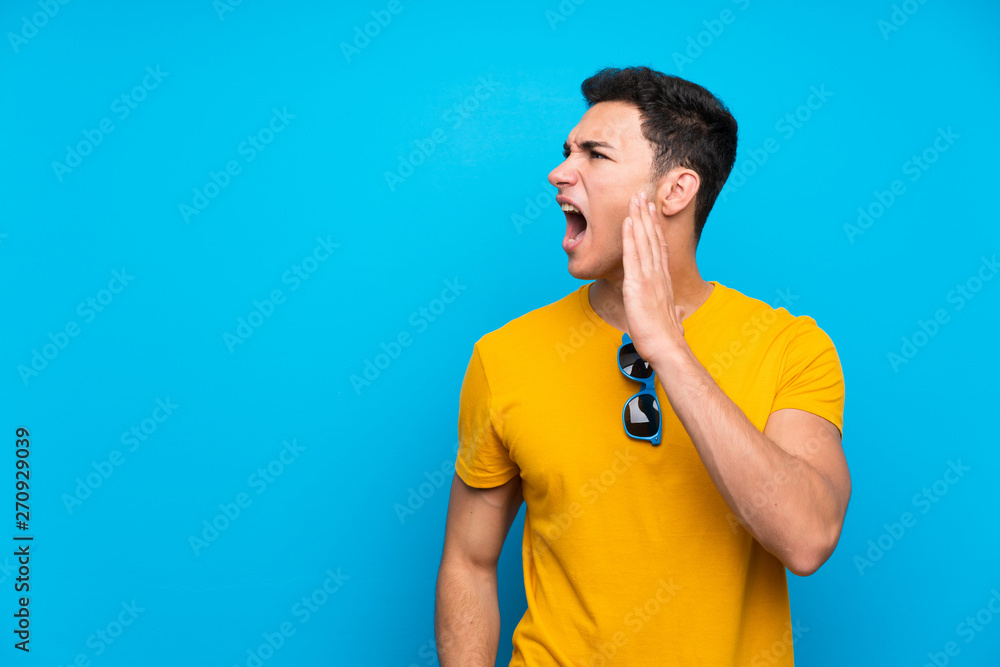 Handsome man over blue background shouting with mouth wide open Handsome man over blue background shouting with mouth wide open