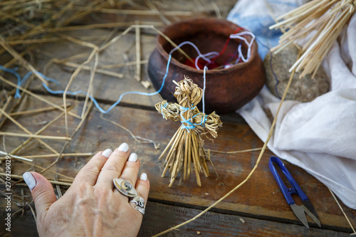 Small figure of a man made of straw, made by the hands of an elderly woman stands on a wooden table photo