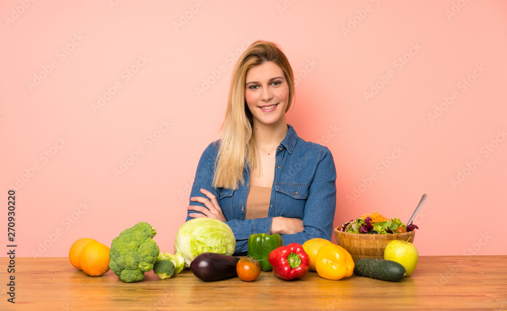 Young blonde woman with many vegetables keeping the arms crossed in frontal position Young blonde woman with many vegetables keeping the arms crossed in frontal position