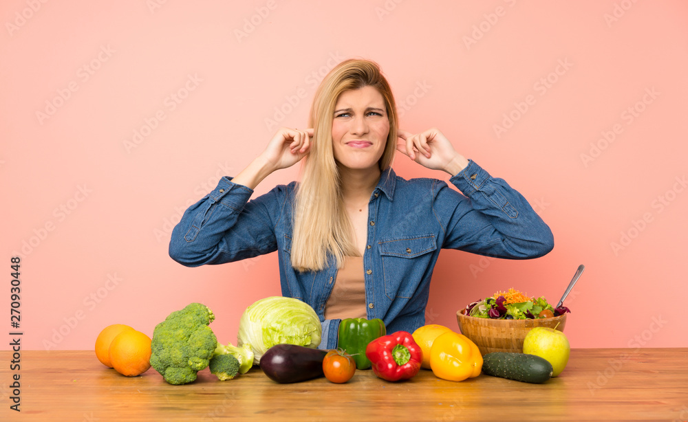 Young blonde woman with many vegetables frustrated and covering ears Young blonde woman with many vegetables frustrated and covering ears