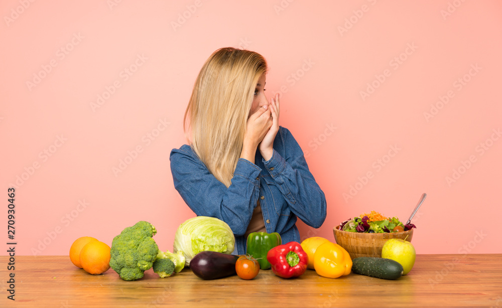 Fototapeta premium Young blonde woman with many vegetables covering mouth and looking to the side