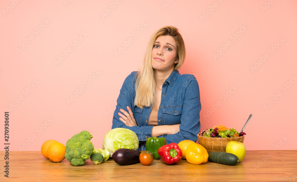 Young blonde woman with many vegetables making doubts gesture while lifting the shoulders Young blonde woman with many vegetables making doubts gesture while lifting the shoulders