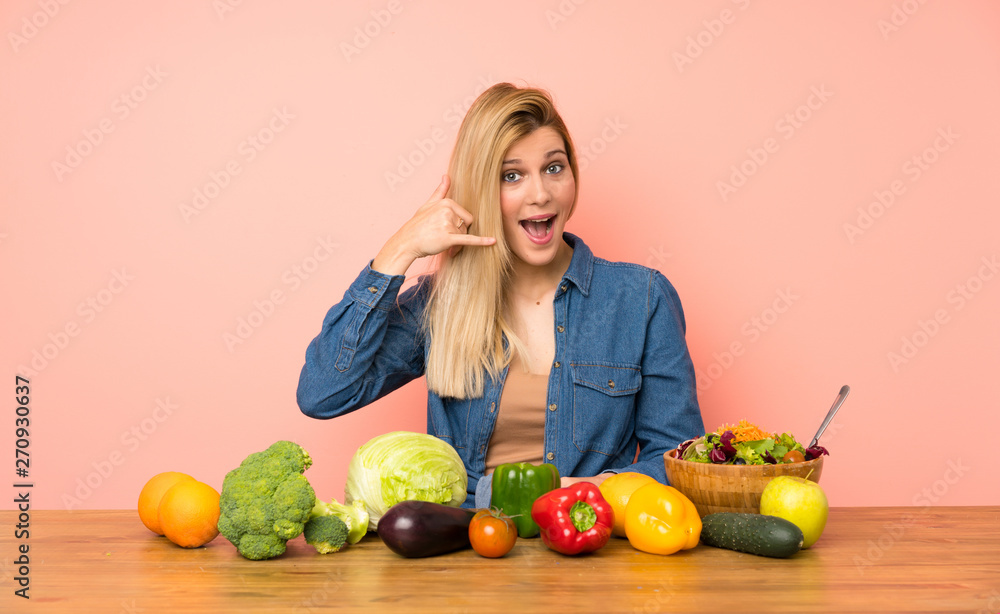 Young blonde woman with many vegetables making phone gesture. Call me back sign Young blonde woman with many vegetables making phone gesture. Call me back sign