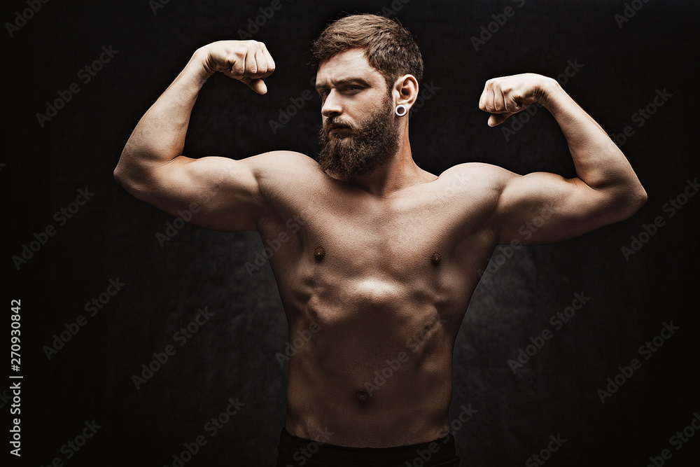Obraz premium Young strong man bodybuilder on the black background. Dark dramatic colors.