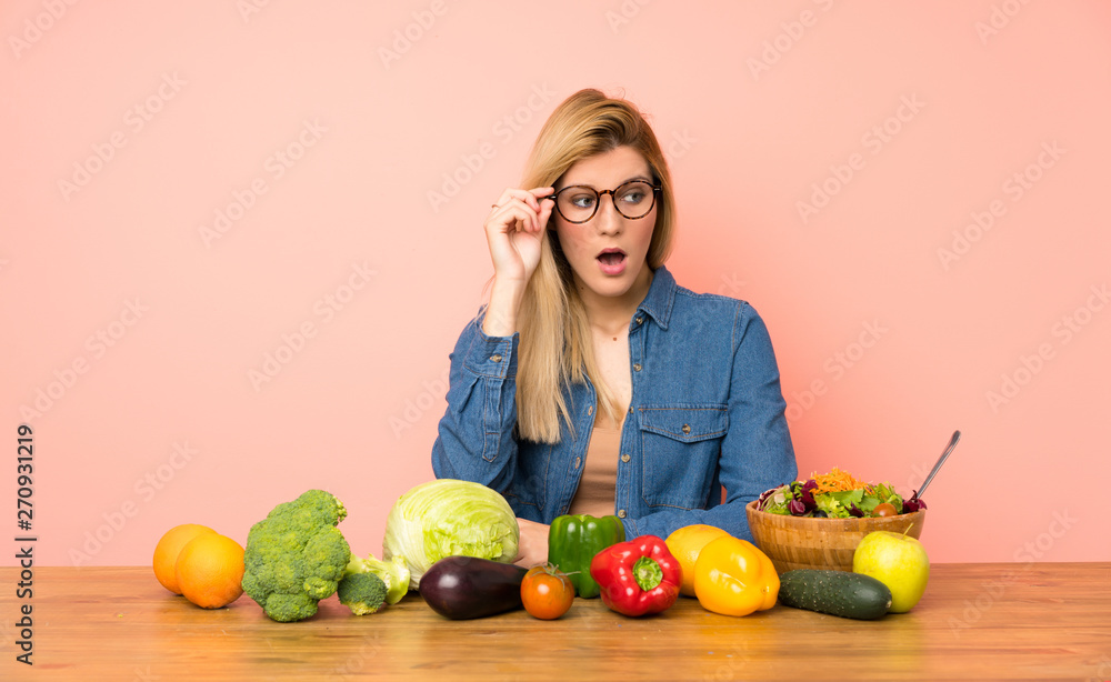 Young blonde woman with many vegetables with glasses and surprised Young blonde woman with many vegetables with glasses and surprised