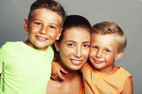 Family values concept. Portrait of fashionable baby boys and their stylish mother in trendy clothing for beach vacation posing over gray background in photostudio, looking at camera. Close up