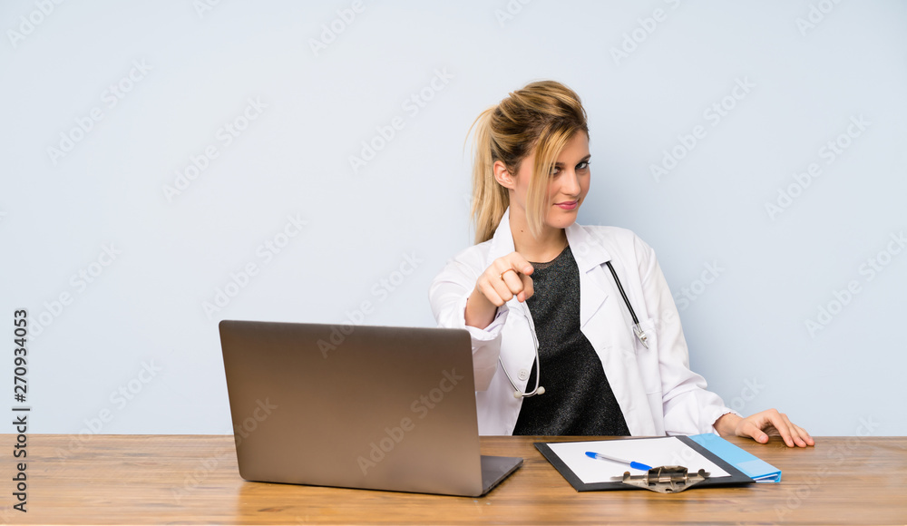 Blonde doctor woman points finger at you with a confident expression Blonde doctor woman points finger at you with a confident expression