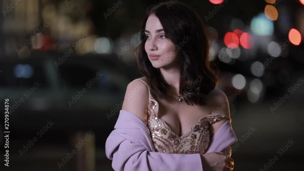 Portrait of beautiful young attractive woman looking at camera in dark city, slow motion. Blurred night background. Portrait of beautiful young attractive woman looking at camera in dark city, slow motion. Blurred night background.