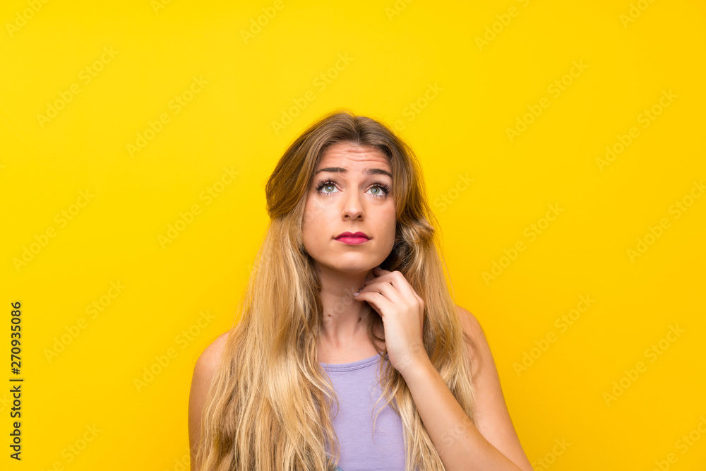 Young blonde woman with overalls over isolated yellow background standing and thinking an idea