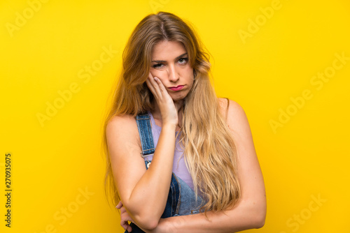 Young blonde woman with overalls over isolated yellow background unhappy and frustrated