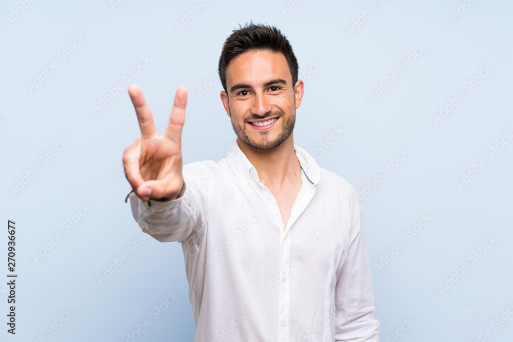 Handsome young man over isolated blue background smiling and showing victory sign Handsome young man over isolated blue background smiling and showing victory sign