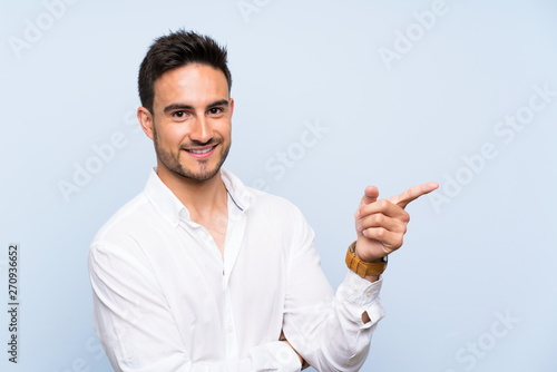 Handsome young man over isolated blue background pointing finger to the side