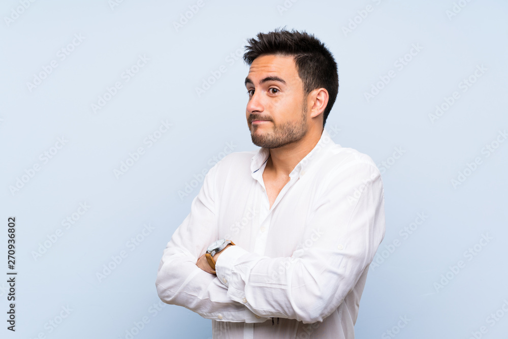 Handsome young man over isolated blue background making doubts gesture while lifting the shoulders Handsome young man over isolated blue background making doubts gesture while lifting the shoulders