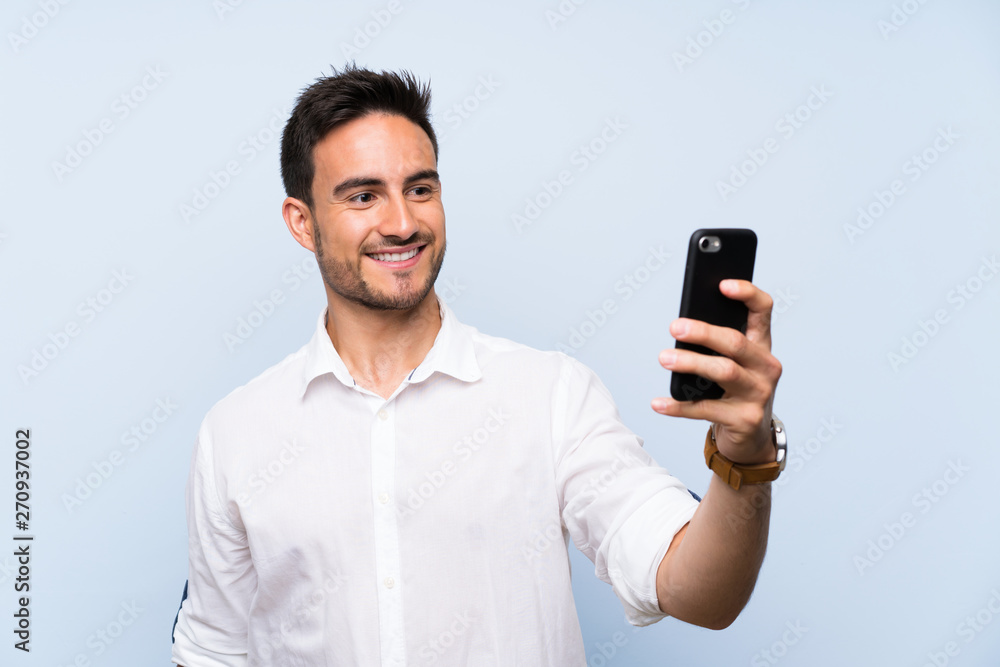Handsome young man over isolated blue background making a selfie Handsome young man over isolated blue background making a selfie