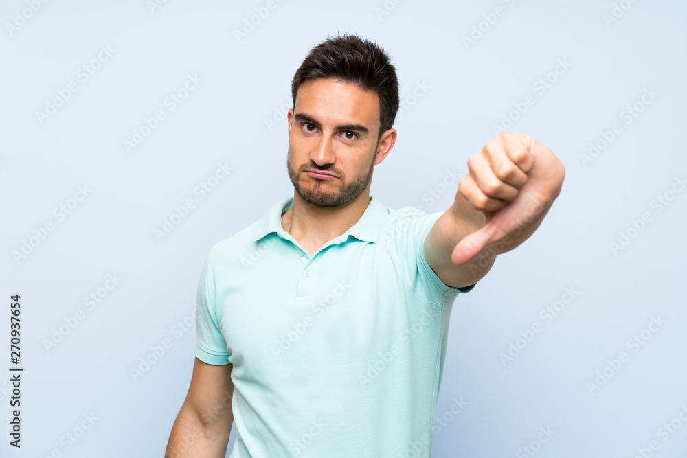 Handsome young man over isolated background showing thumb down with negative expression Handsome young man over isolated background showing thumb down with negative expression