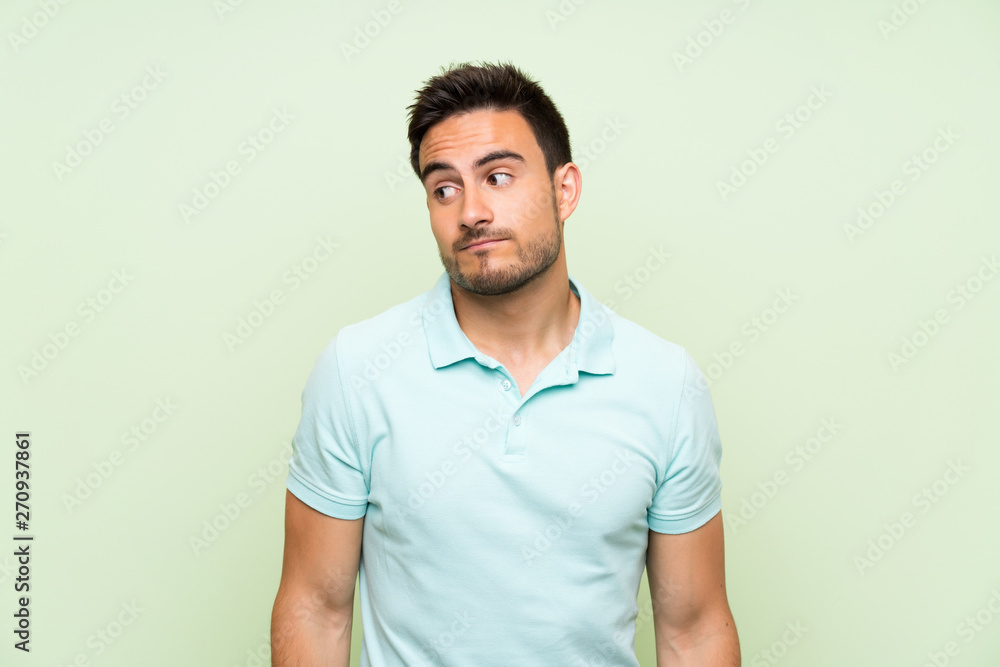 Handsome young man over isolated background making doubts gesture looking side Handsome young man over isolated background making doubts gesture looking side