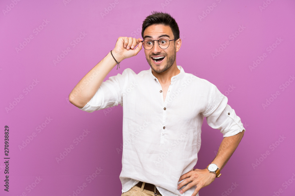 Handsome young man over isolated background with glasses and surprised Handsome young man over isolated background with glasses and surprised