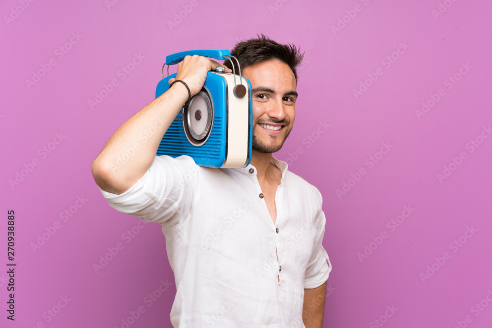 Fototapeta premium Handsome young man over purple background holding a radio