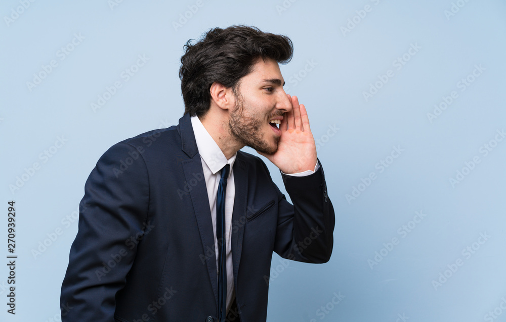 Businessman over isolated blue wall shouting with mouth wide open to the lateral Businessman over isolated blue wall shouting with mouth wide open to the lateral