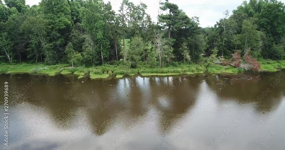 An aerial view or drone shot of a man-made fishing lake set amidst forested trees and manicured lawns in a private property. An aerial view or drone shot of a man-made fishing lake set amidst forested trees and manicured lawns in a private property.