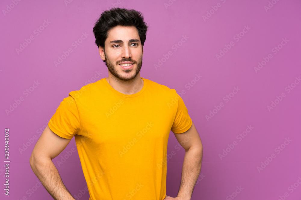 Handsome over isolated purple wall posing with arms at hip and smiling Handsome over isolated purple wall posing with arms at hip and smiling