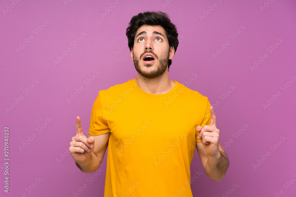 Handsome over isolated purple wall surprised and pointing up Handsome over isolated purple wall surprised and pointing up