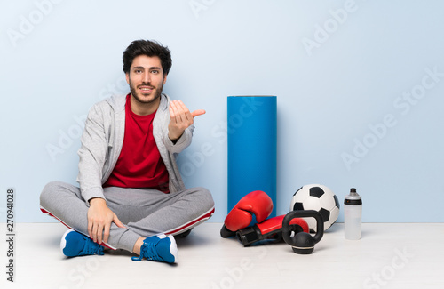 Sport man sitting on the floor inviting to come with hand. Happy that you came