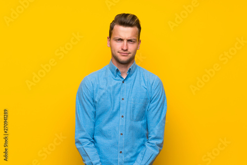 Blonde man over isolated yellow wall with sad and depressed expression © luismolinero