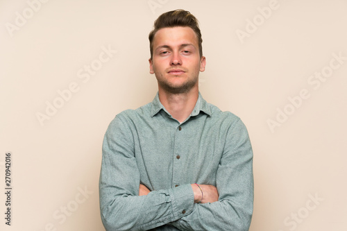 Blonde handsome man over isolated wall keeping arms crossed
