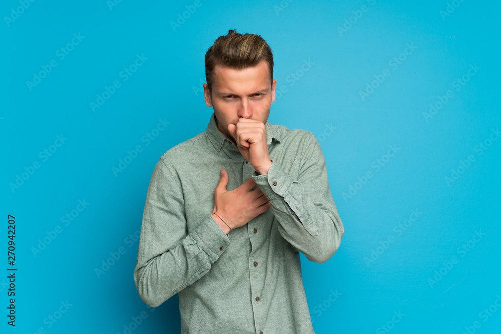Blonde man over isolated blue wall is suffering with cough and feeling bad Blonde man over isolated blue wall is suffering with cough and feeling bad