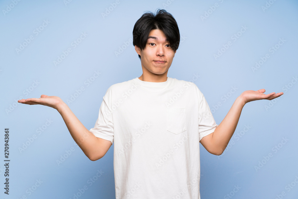 Asian man on isolated blue background having doubts with confuse face expression Asian man on isolated blue background having doubts with confuse face expression