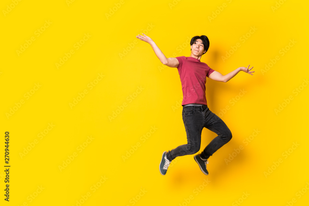 Asian man jumping over isolated yellow wall